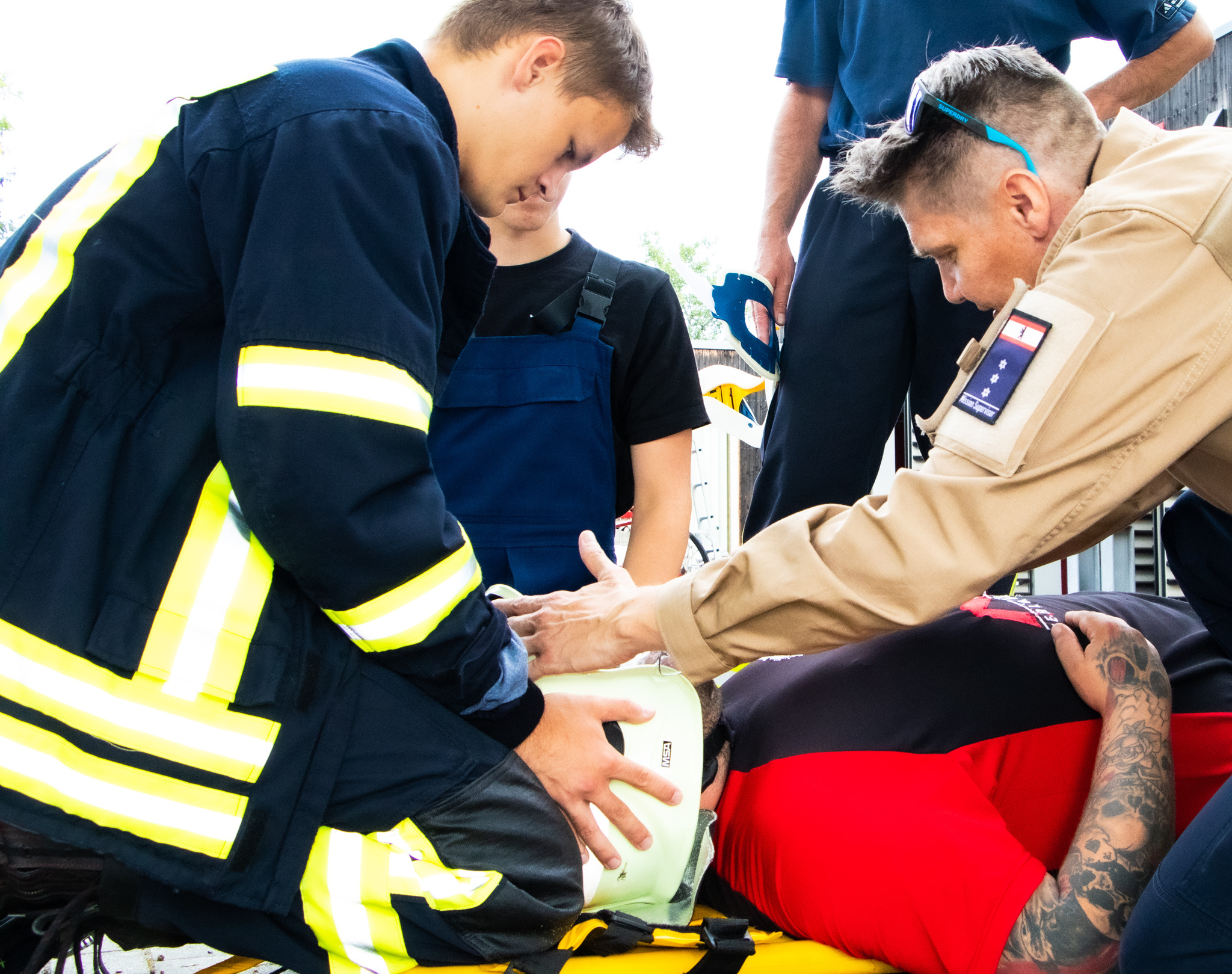 Mehrere Männer in Feuerwehrkleidung versorgen einen am Boden liegenden Mann mit Helm.