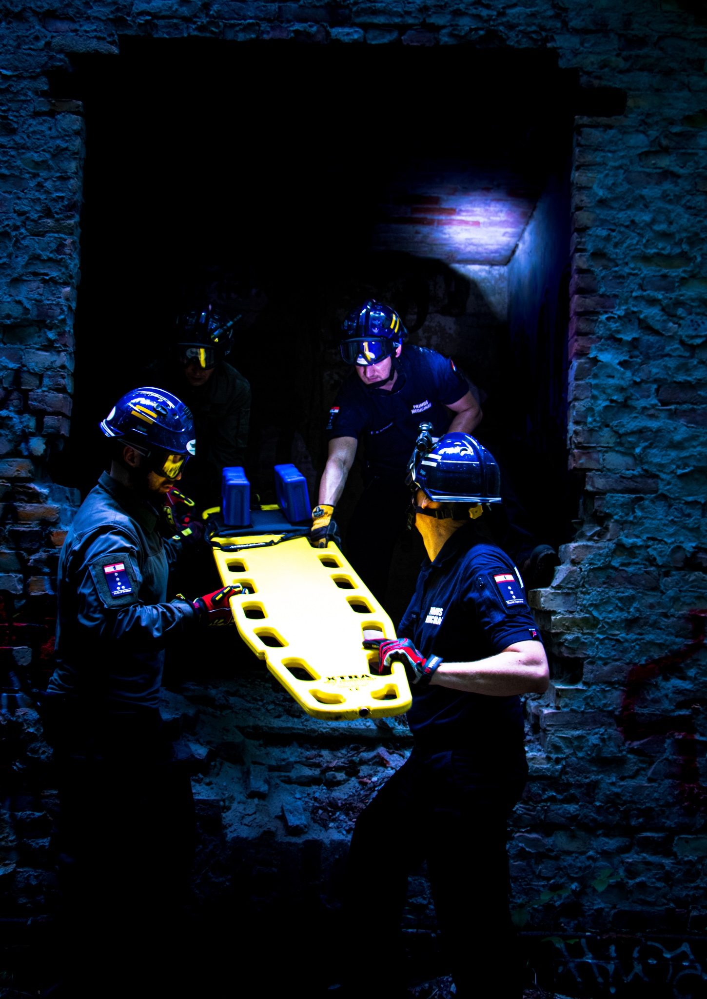 Einsatz bei Dunkelheit: Vier Personen bugsieren eine Patiententrage ins Innere einer Ruine. Alle tragen Uniformen und Schutzhelme mit Stirnlampen.